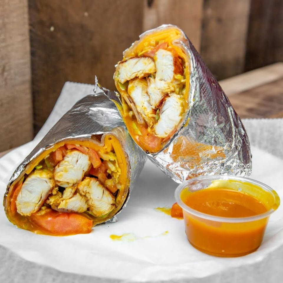Two chicken wraps with orange sauce and vegetables, partially unwrapped from foil, with a side of dipping sauce.