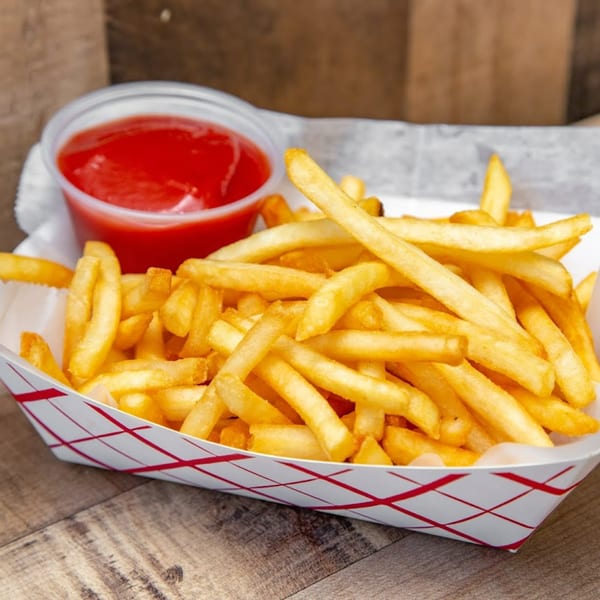 Golden french fries in a paper tray with a side of ketchup on a wooden surface.
