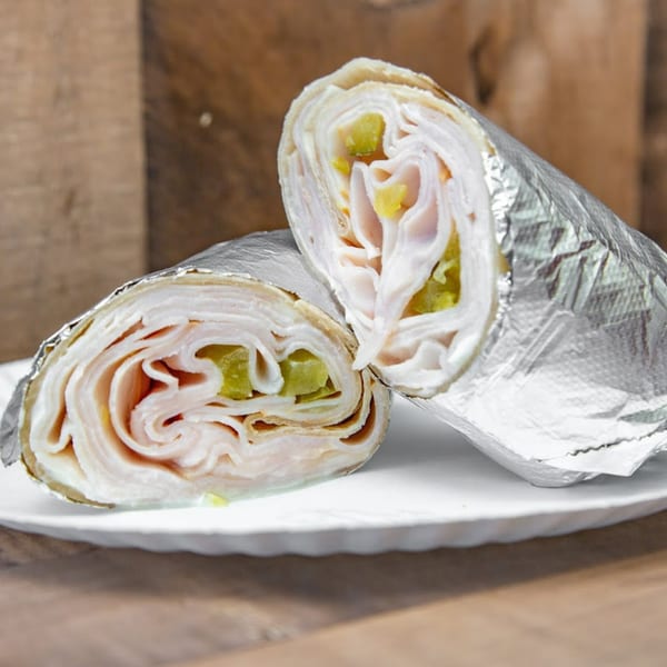 Two halves of a turkey and pickle wrap, partially unwrapped from foil, on a white plate.