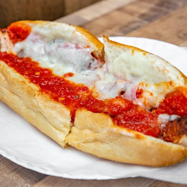 Mama Gina's Pizzeria meatball sub with melted mozzarella cheese and marinara sauce on a white plate.