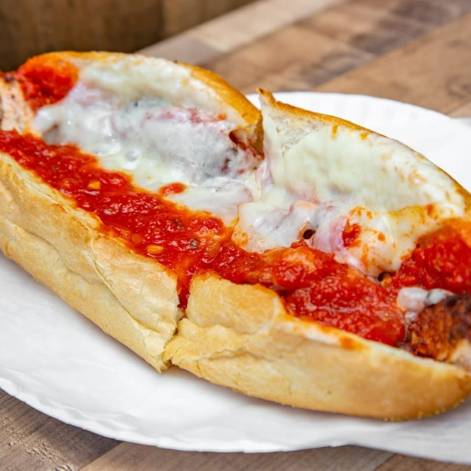 Mama Gina's Pizzeria meatball sub with melted mozzarella cheese and marinara sauce on a white plate.