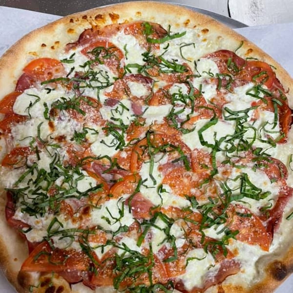 Mama Gina's Pizzeria pizza with sliced tomatoes, melted mozzarella, and fresh basil.