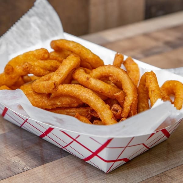 Golden brown curly fries in a white paper tray with red crisscross lines on a wooden table.